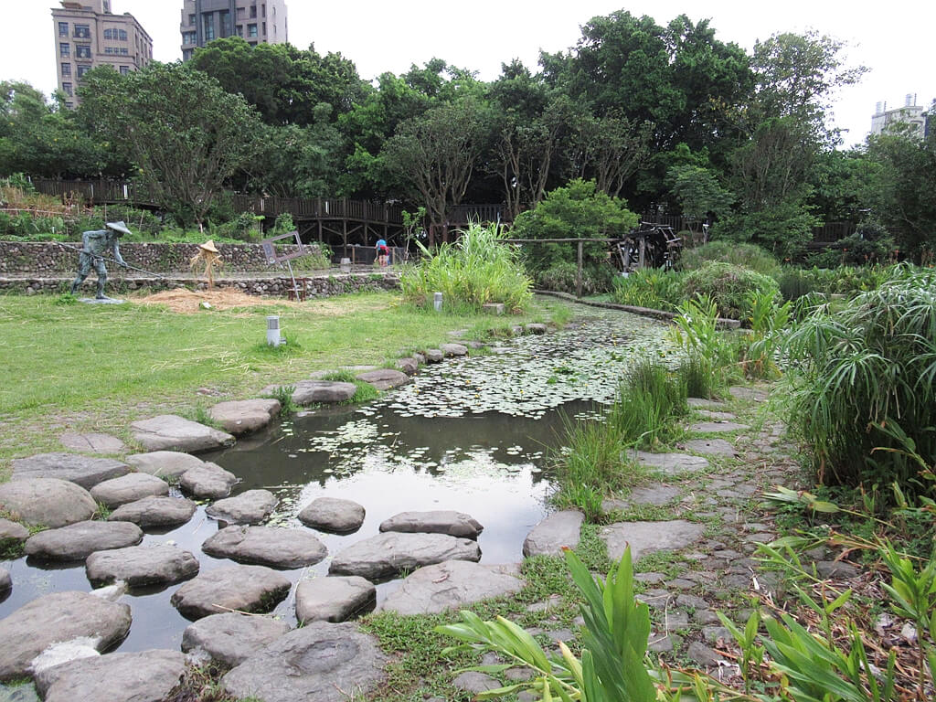 臺北市客家文化主題公園的圖片：小河流以及農人整理稻草、水車